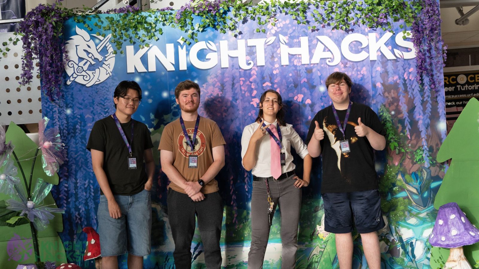 Matthew, second from left in a brown shirt, with three other students in front of the KnightHacks backdrop at UCF